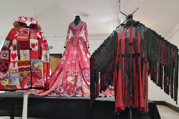 The Red Dress is flanked by the Community Shawl, and to the right by the Dress with black ribbons with the names of 100 murdered women