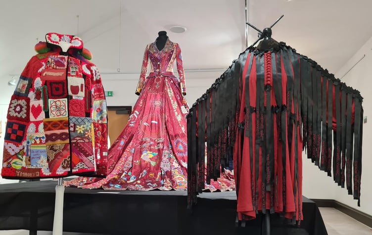 The Red Dress is flanked by the Community Shawl, and to the right by the Dress with black ribbons with the names of 100 murdered women