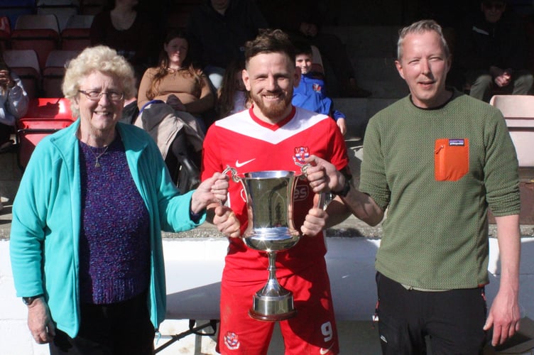 Knighton Town skipper Luke Boundford receives the trophy from Mrs Lynda Eaton, with her son Daryl Eaton (Image: Barcud-Coch Photography)